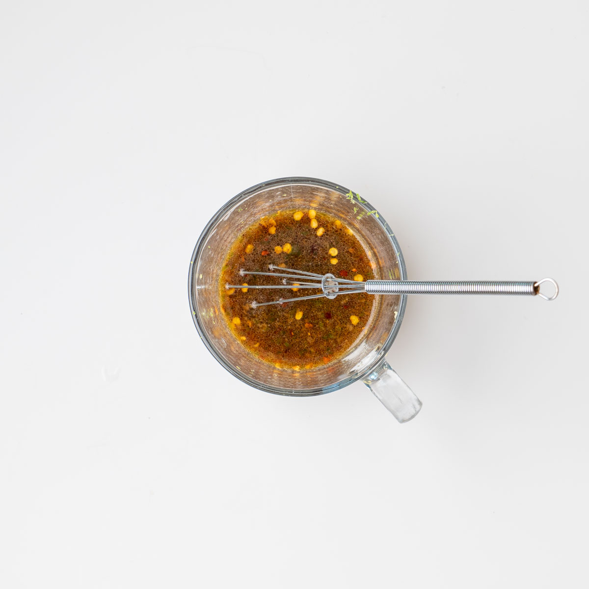 Overhead flat lay of zesty lime, tamari, and ginger salad dressing being whisked in a glass measuring cup on a white surface