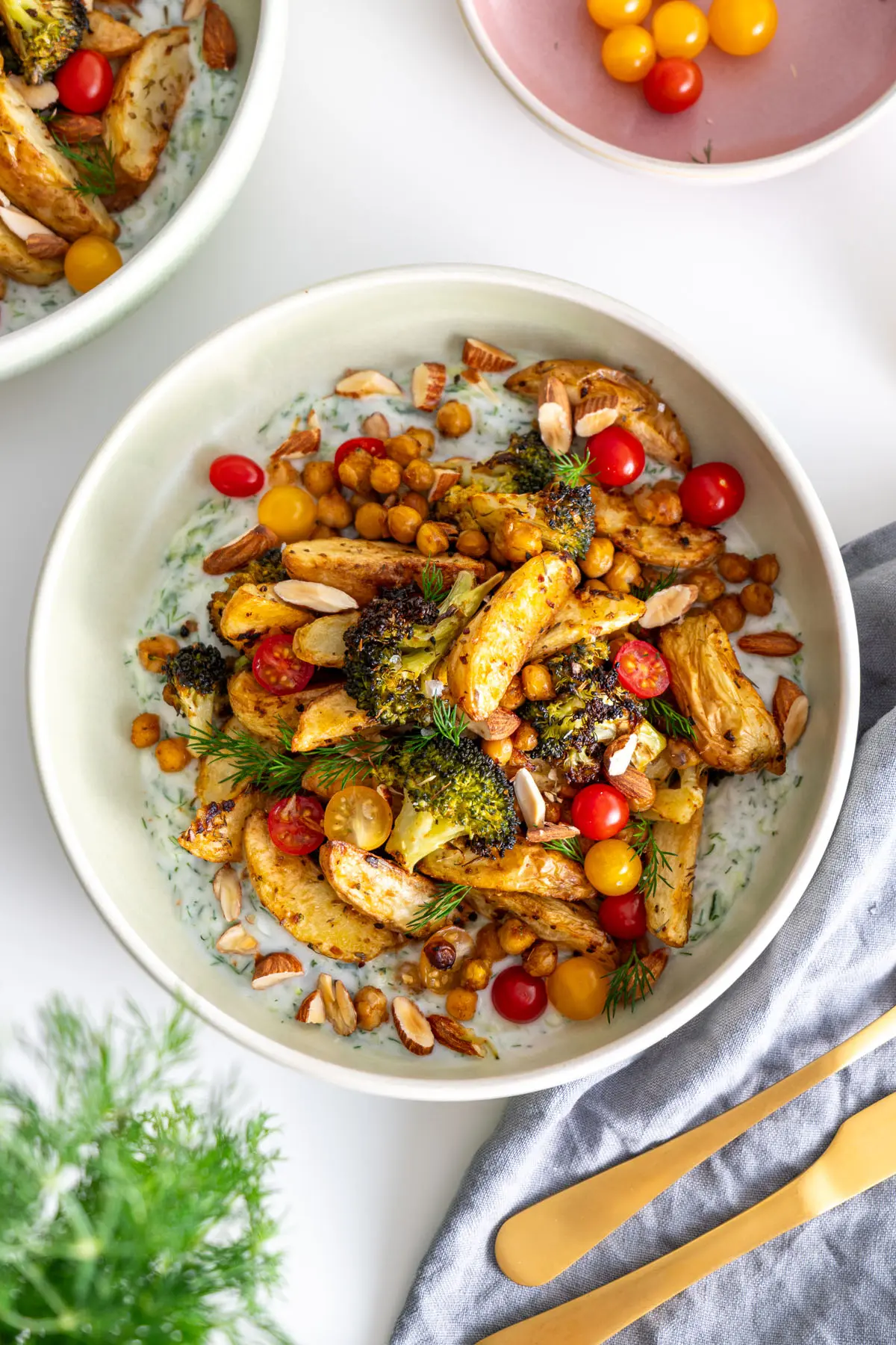 A close-up of a bowl with roasted potatoes, broccoli, and chickpeas on a bed of tzatziki.