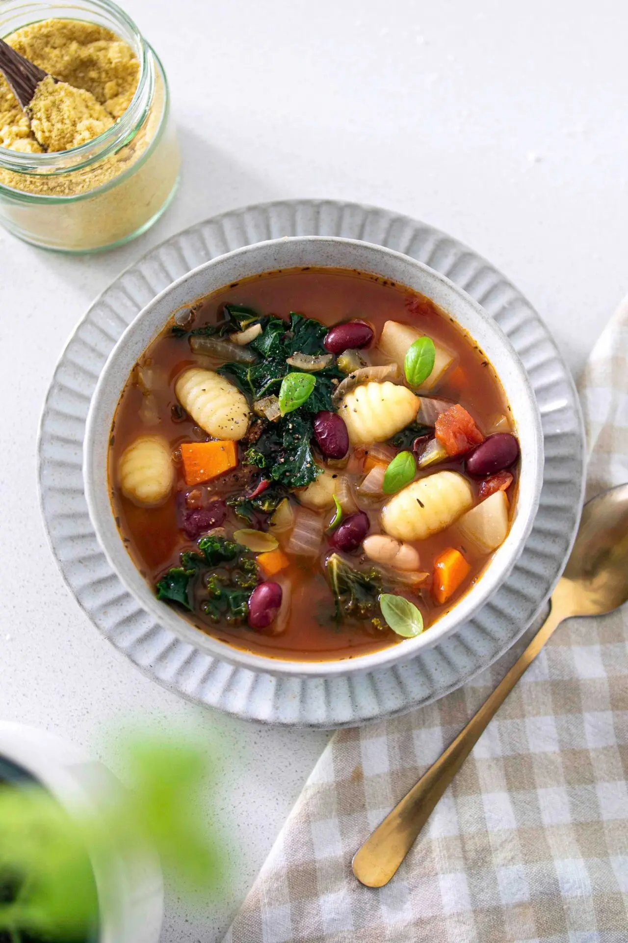 A bowl of hearty minestrone soup filled with vegetables, beans, and pasta, topped with a sprinkle of vegan cheese.