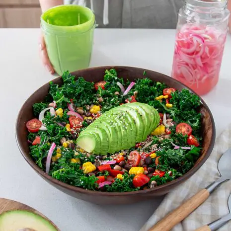 2-Bean avocado salad in a big wooden salad bowl with a jar of vibrant green dressing