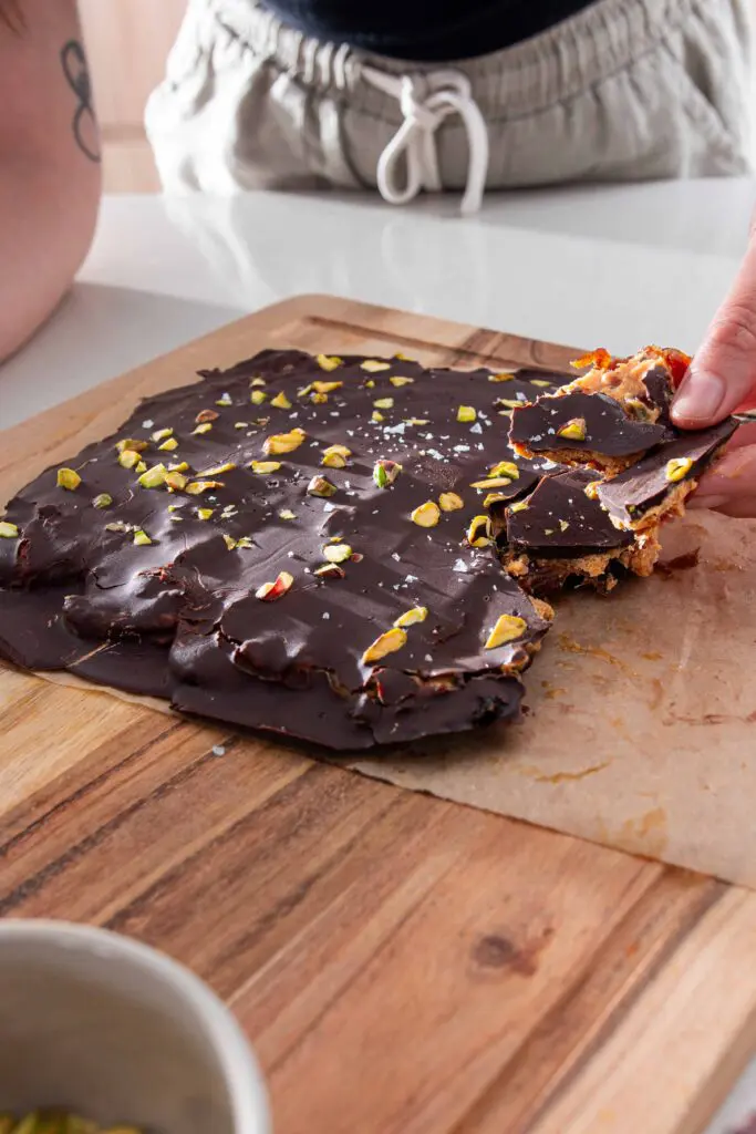 Slab of dark chocolate date park topped with pistachios on a wooden chopping board