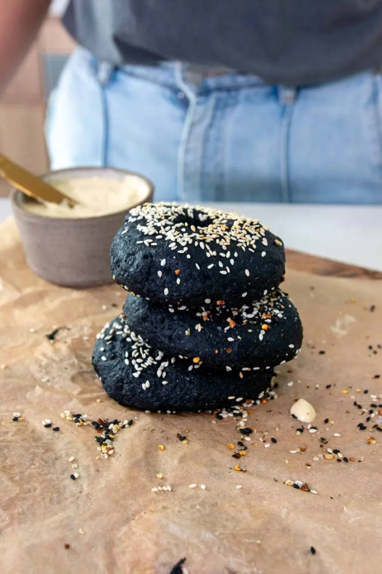 Fresh homemade charcoal vegan bagels stacked on top of each other on a sheet of baking paper