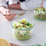Tupperware container full of layers of vibrant veggies and a green creamy sauce