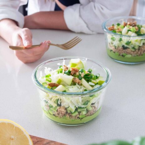 Tupperware container full of layers of vibrant veggies and a green creamy sauce