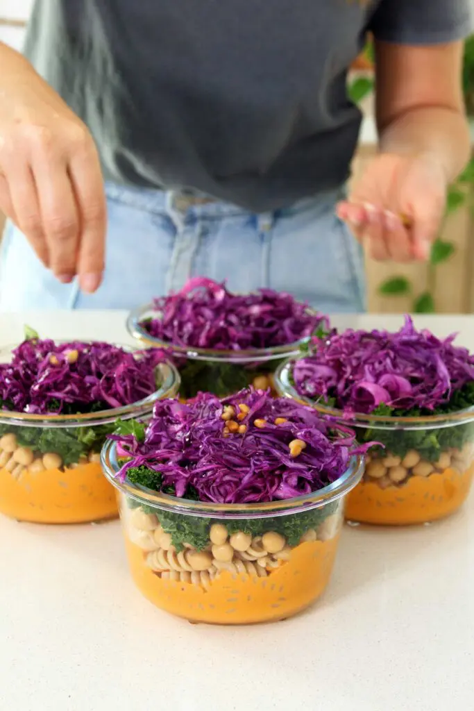 Adding the toasted pine nuts to the Romesco pasta salad meal prep containers