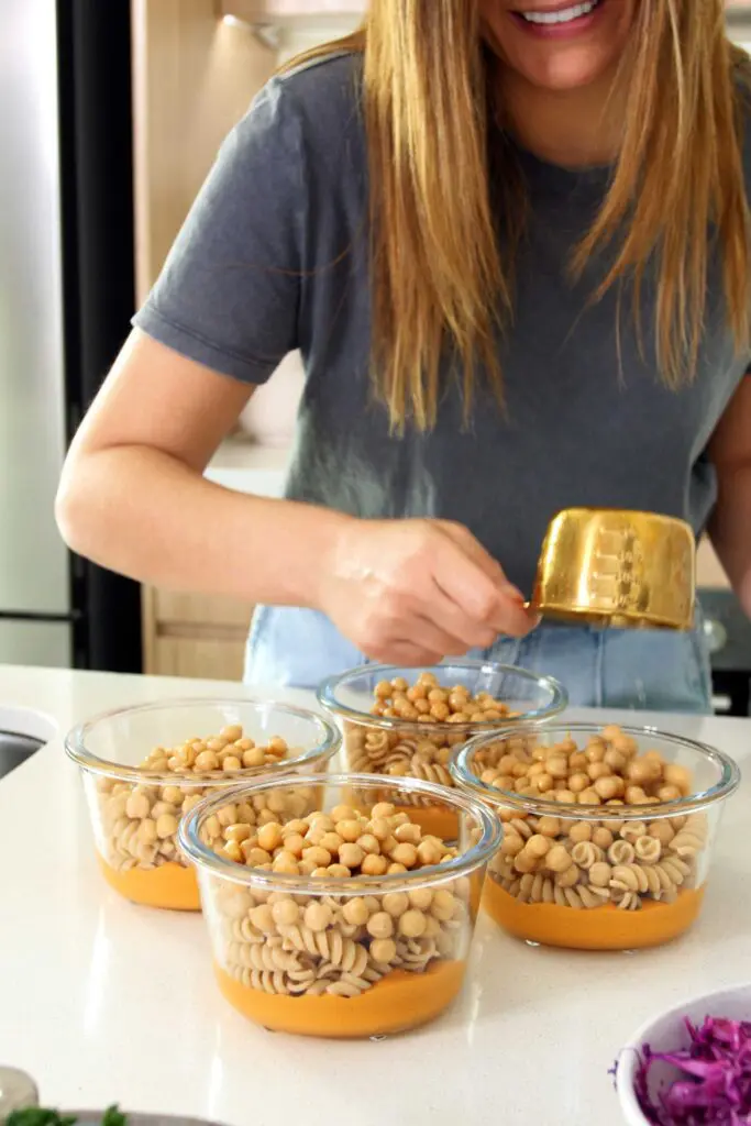 Adding the chickpeas to the Romesco pasta salad meal prep containers