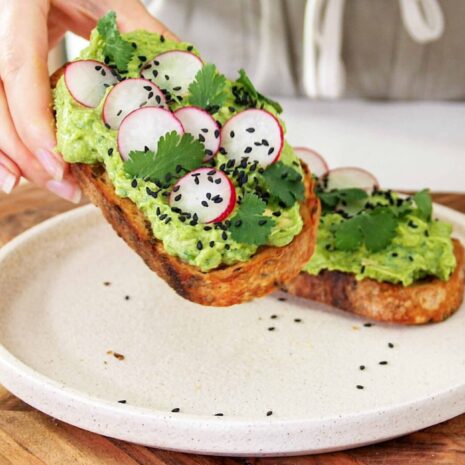 Sarah holding a Smashed peas and avocado toast on a white plate on a wooden serving board
