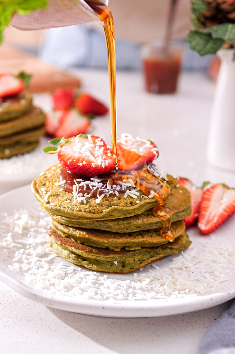 Maple syrup pouring over a vibrant green stack of Matcha Avocado Gluten-Free Christmas Pancakes