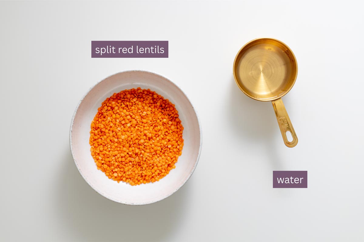 Split red lentils in a white bowl and water in a golden measuring cup