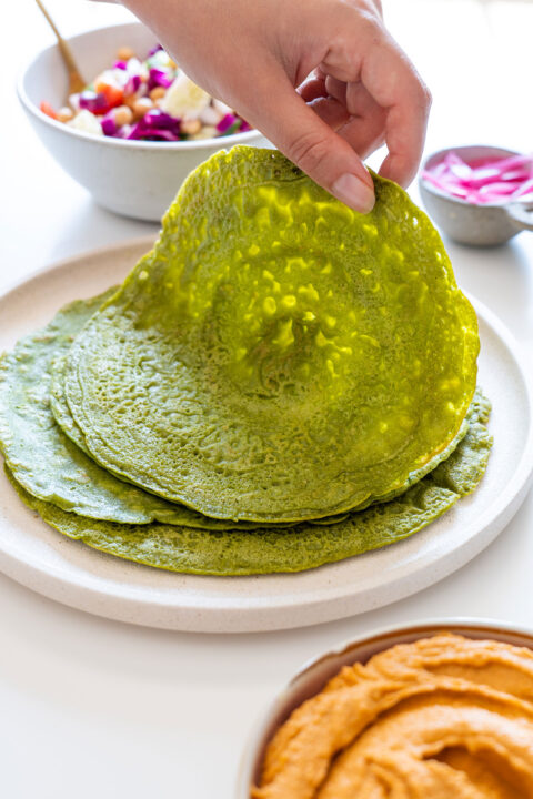Image of a hand picking up a fresh, green buckwheat spinach wrap, showcasing its flexibility and texture.