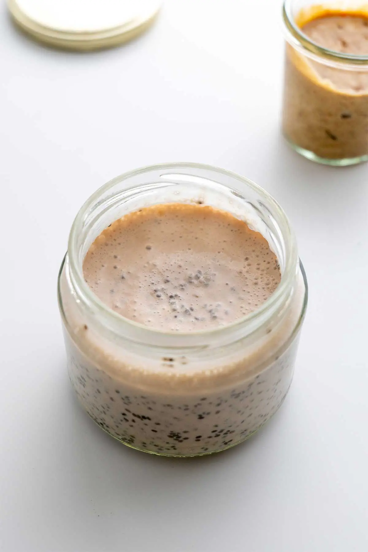 The prepping stage of Banoffee Chia Pudding with a clear jar half-filled with chia mixture before being chilled and the addition of toppings.