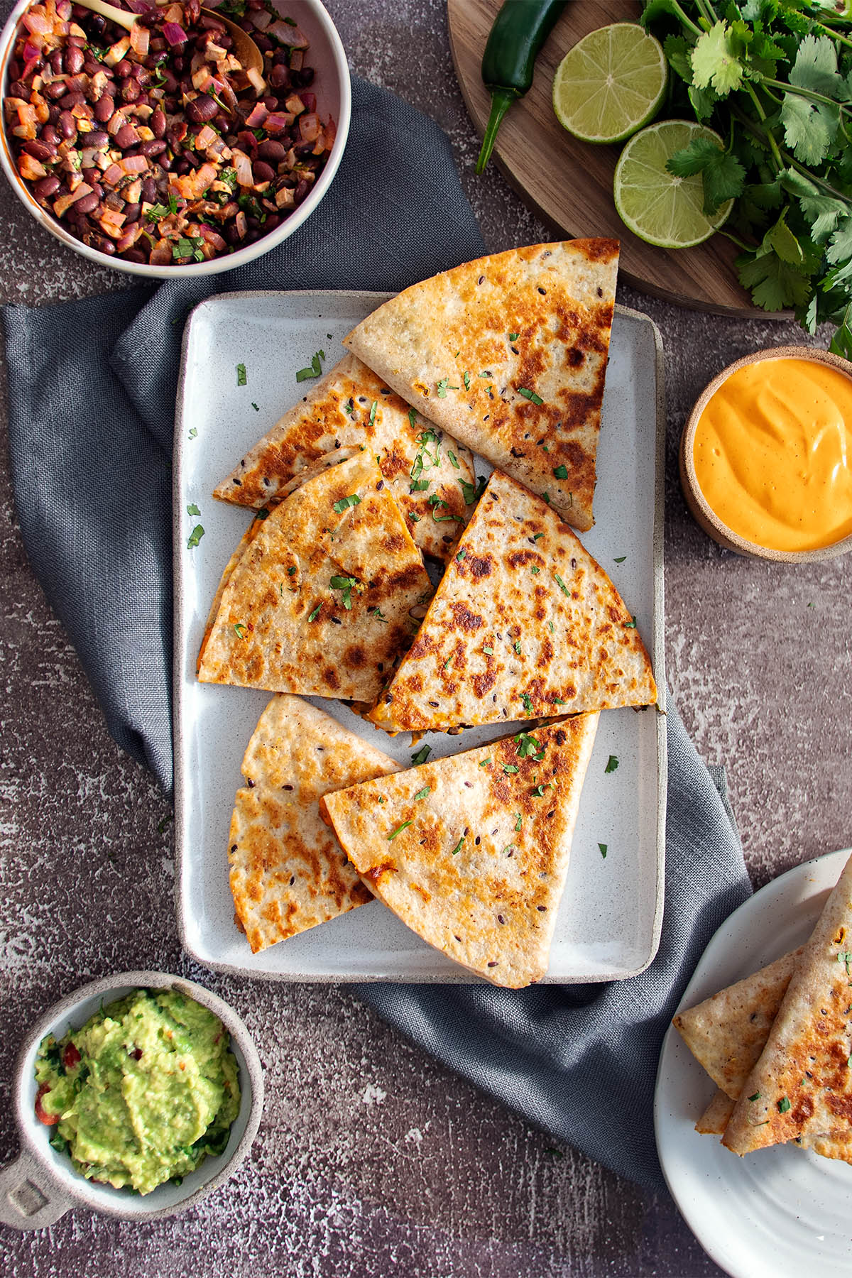 A plate with quesadillas surrounded by various condiments as featured in The Ultimate Plant-Based Cookbook by Sarah Cobacho