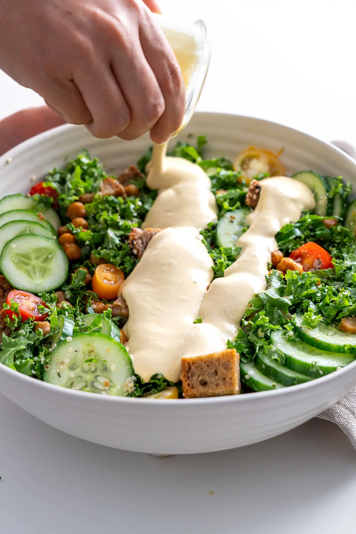 Creamy vegan Caesar dressing being poured onto a High-Protein Kale Salad.