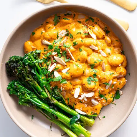 Serving of High-Protein Romesco Butter Beans with garnished parsley and side of broccolini on a clean white background.