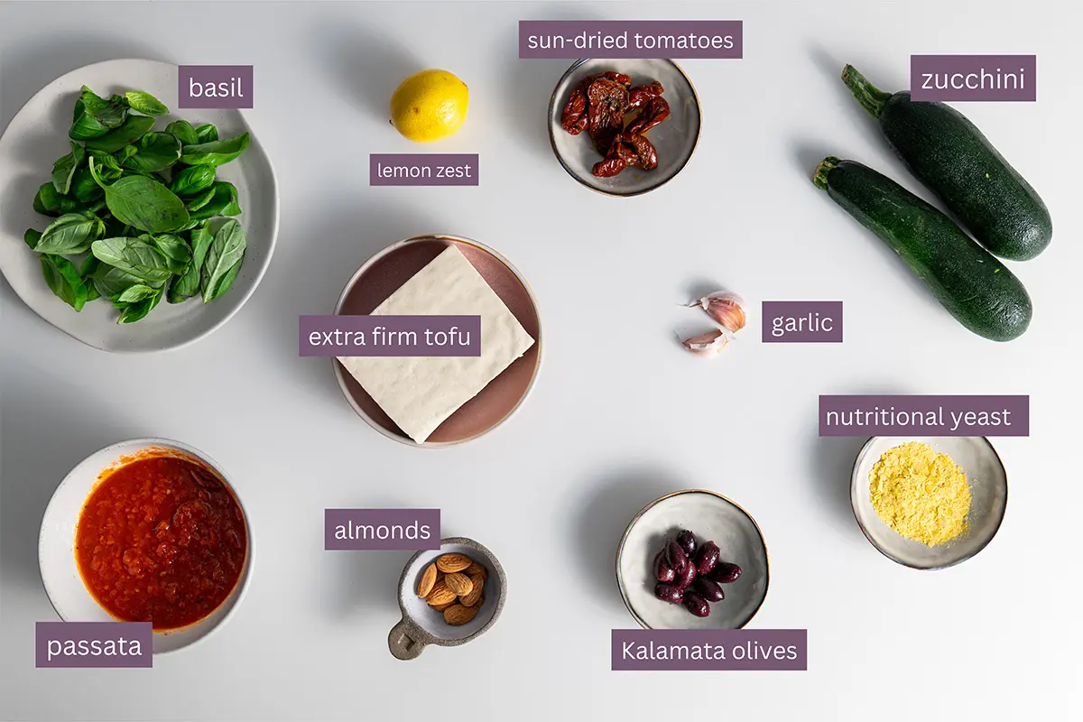 Vibrant ingredients for a Mediterranean recipe on a white surface, including fresh produce and condiments.