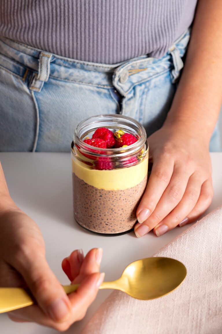 Close-up of a Sarah Cobacho holding a Chocolate Pistachio Chia Pudding in a glass jar, ready to eat.