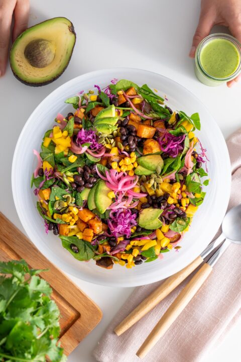 Overview of a colorful sweet potato salad served in a large white bowl on a white table.