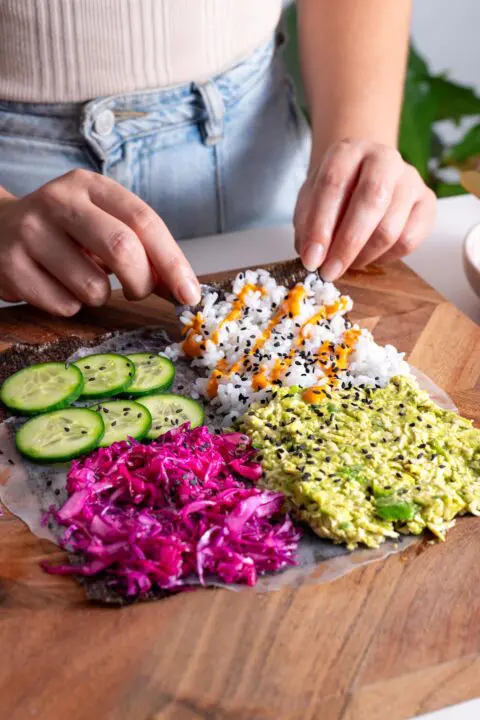 Hands folding a colorful veggie sushi wrap filled with fresh ingredients
