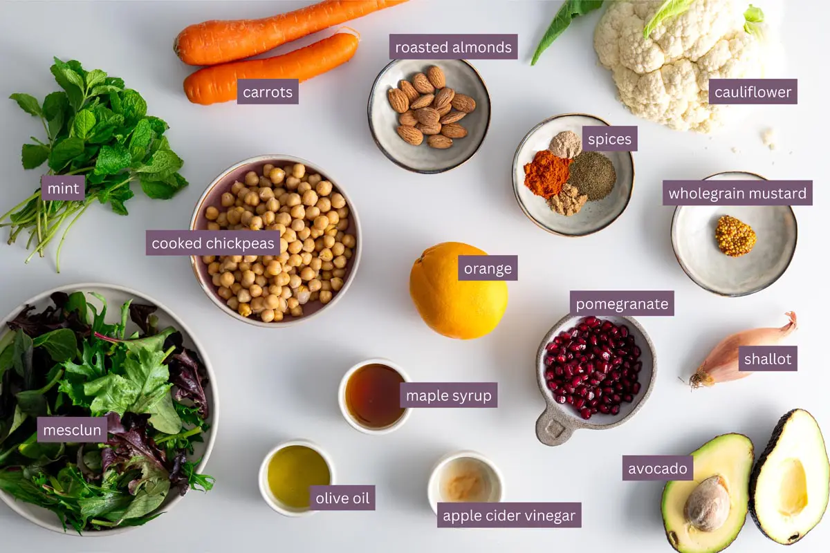 Vibrant ingredients for a spiced roasted cauliflower and chickpea salad on a white surface.