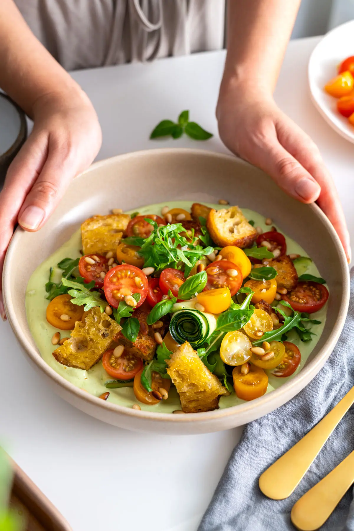 Sarah's hands holding a bowl of freshly made high-protein pesto bowl with vibrant ingredients.