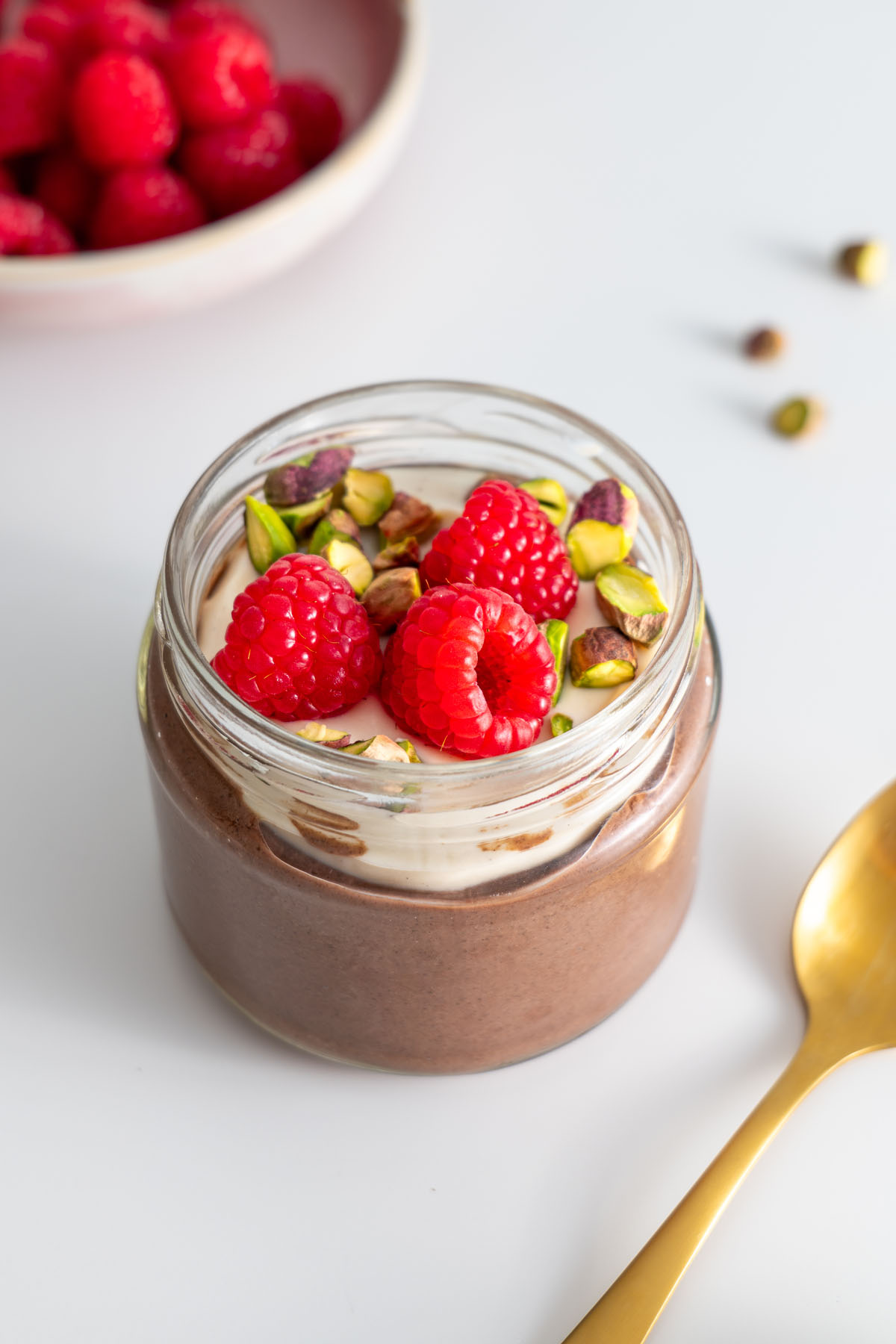 Pudding cacao chia phủ sữa chua đậu nành, quả mâm xôi và quả hồ trăn trong lọ thủy tinh.