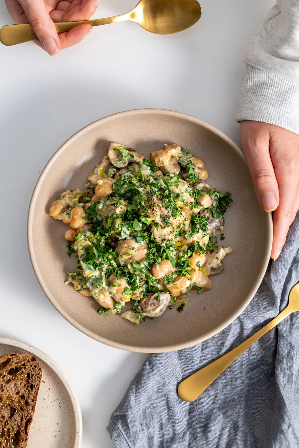 Top-down view of creamy miso butter beans with kale served in a bowl with gold cutlery.