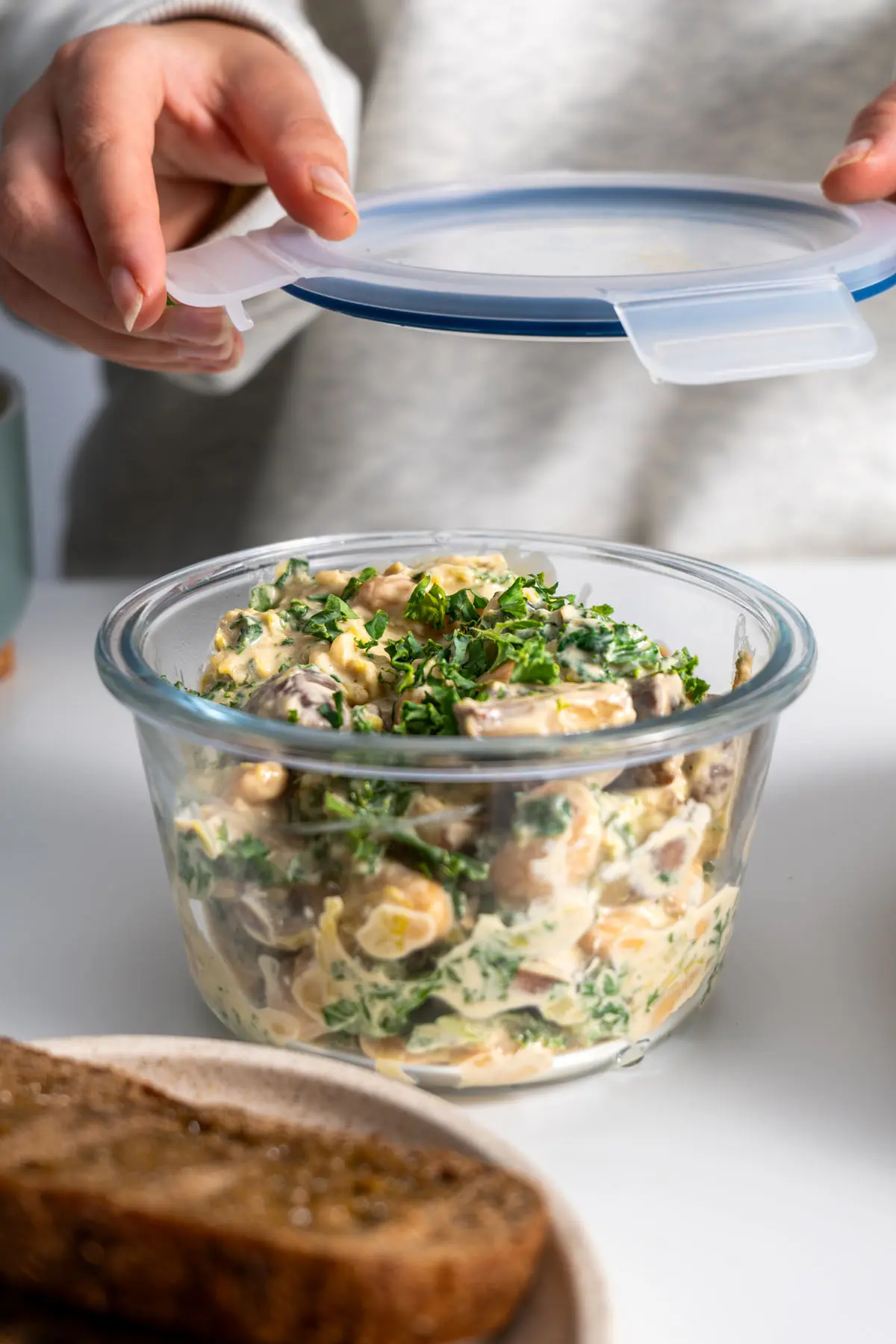 Sarah Cobacho preparing to store creamy miso butter beans with kale in a glass container.