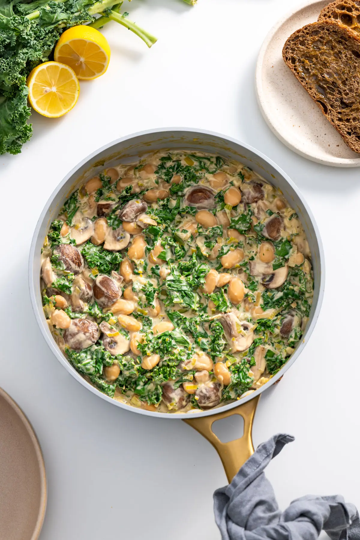 Creamy miso butter beans with kale in a cooking pan next to lemon and toasted bread.