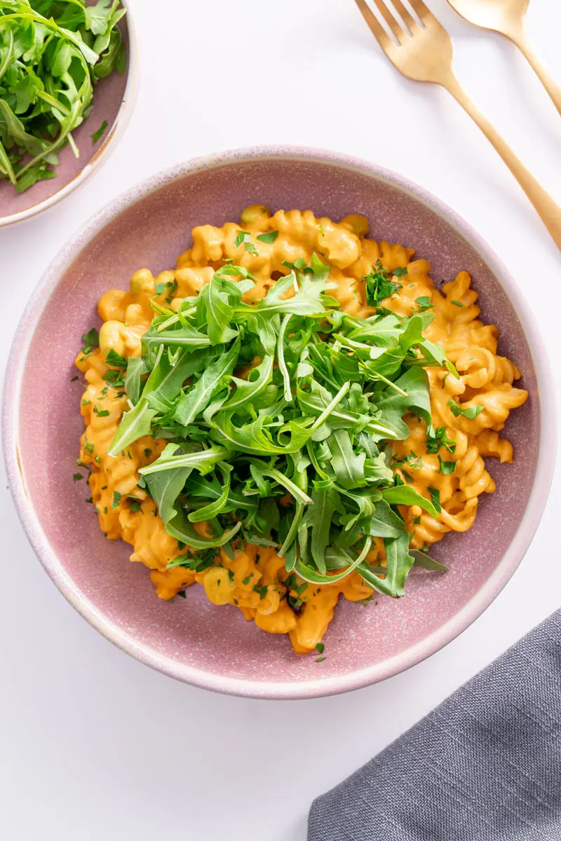 Creamy high protein pumpkin pasta served in a pink bowl, topped with fresh rocket