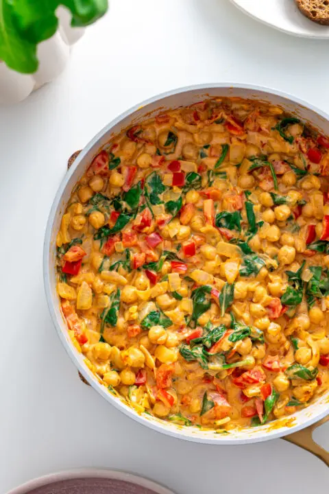 Pan filled with cooked Marry Me Chickpeas with spinach and red bell pepper.