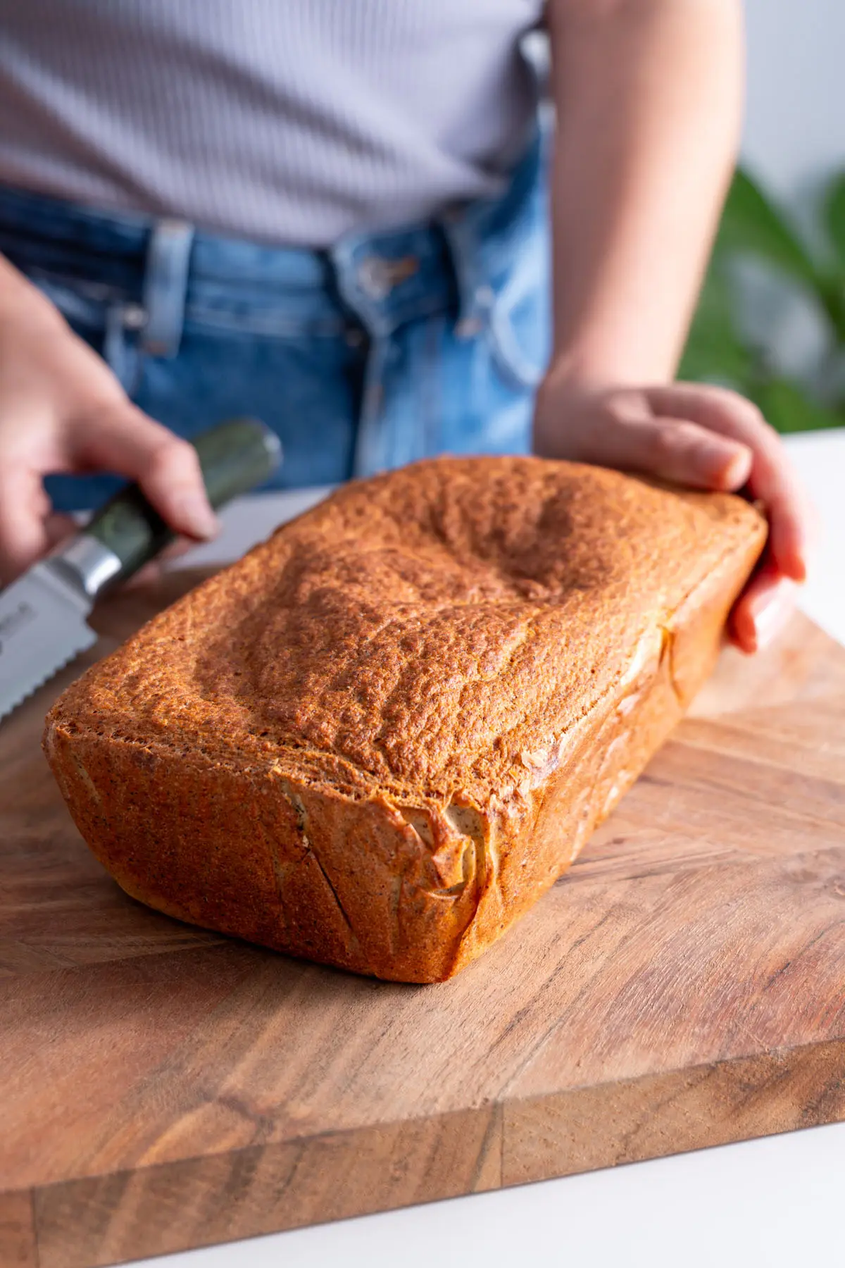 Sarah Cobacho about to slice a loaf of red lentil quinoa bread on a wooden board.