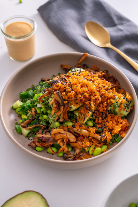Close-up of crispy rice salad with gochujang mushrooms, cucumber, avocado, and edamame in a bowl.