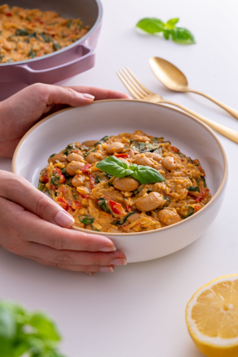Sarah Cobacho holding a bowl of creamy orzo with butter beans and basil, ready to eat.