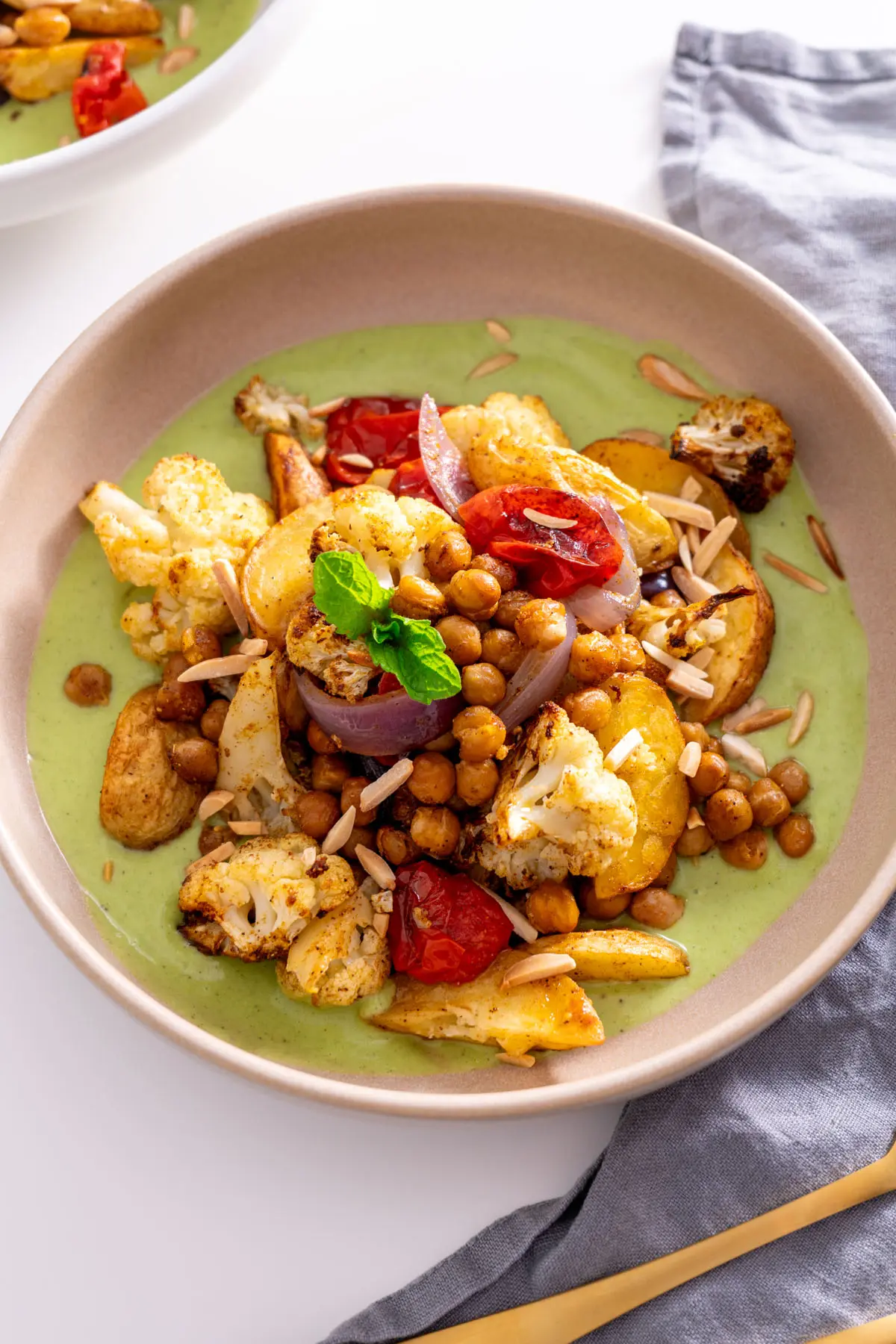 A serving of curry baked veggies with raita sauce, topped with mint and slivered almonds.