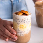 Sarah Cobacho holding a glass of Banoffee Overnight Oats, topped with banana slices and pecans.