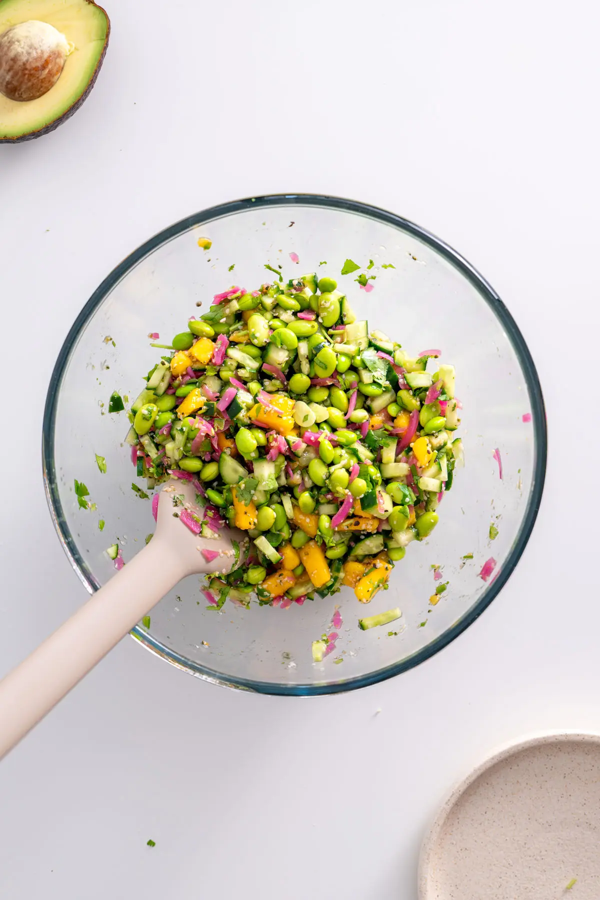 Close-up of the colorful topping mix with edamame, mango, cucumber, and pickled onions in a mixing bowl.