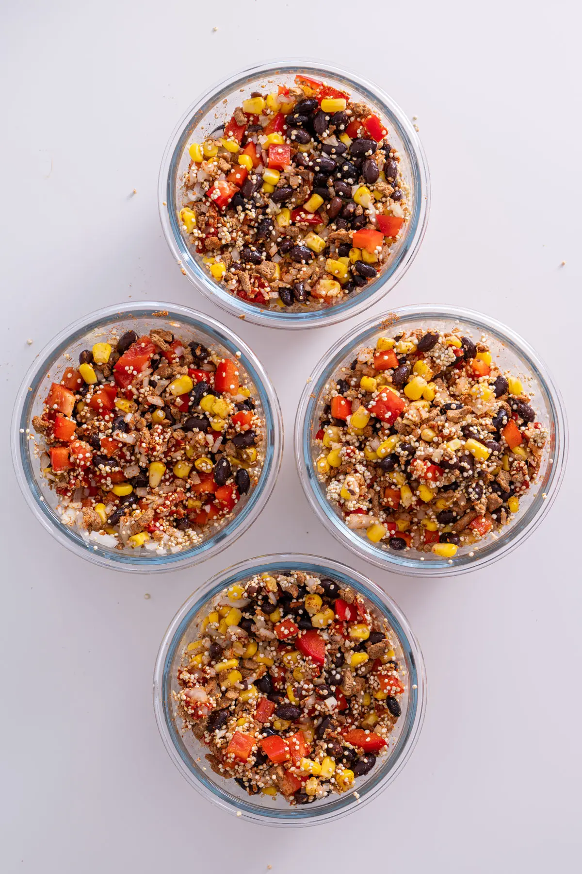 Overhead view of four burrito bowls filled with ingredients including black beans, corn, and quinoa before baking.
