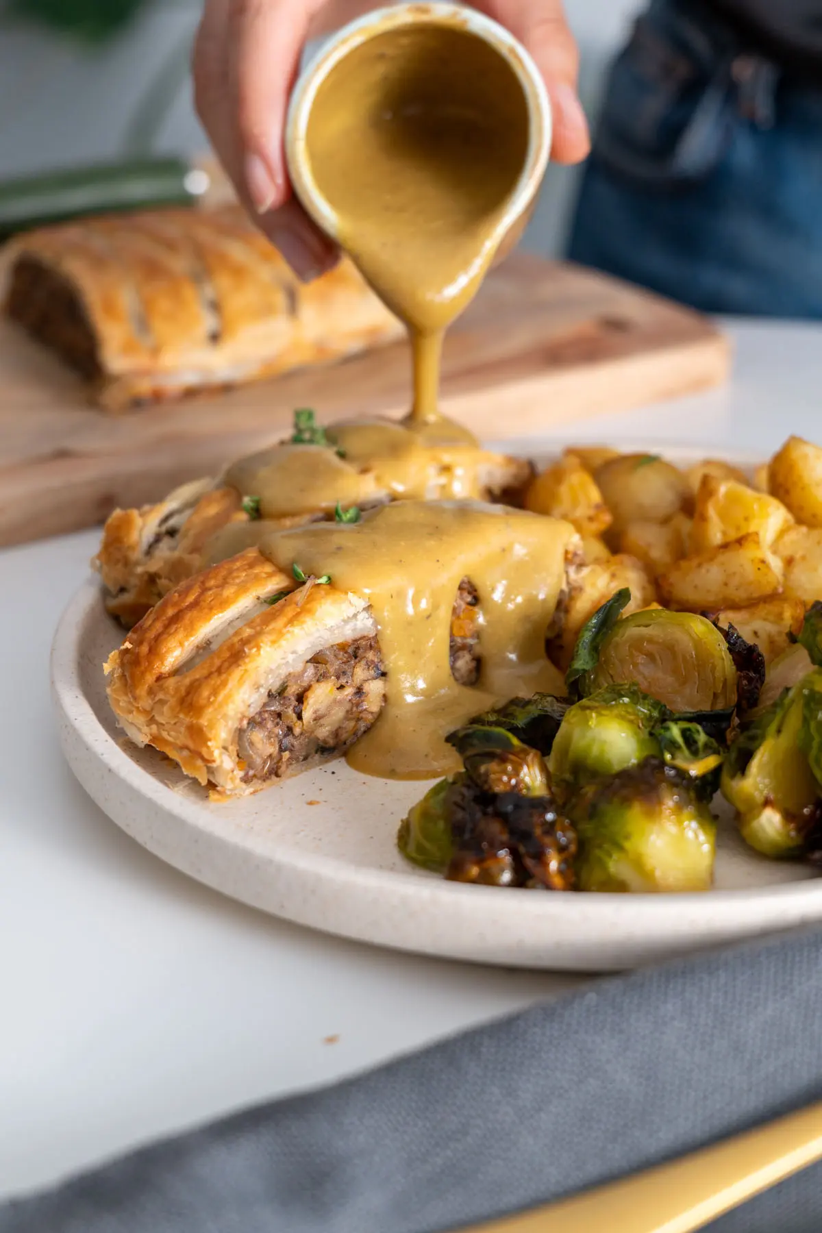 Sarah Cobacho pouring vegetable gravy over vegan mushroom Wellington slices on a plate of roasted vegetables.