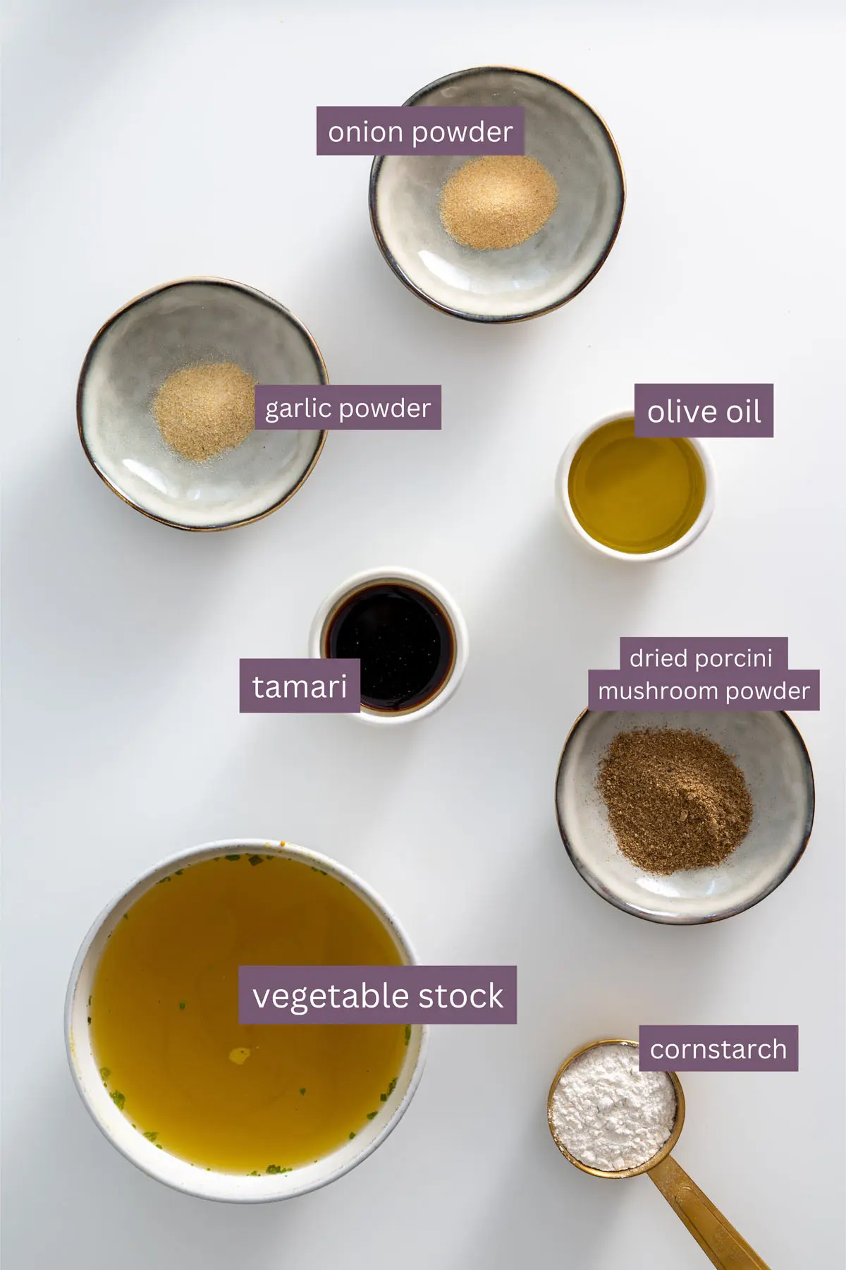 Ingredients for a vegan gravy with rich vegetable stock, including tamari, porcini mushroom powder, and cornstarch, displayed on a white background.