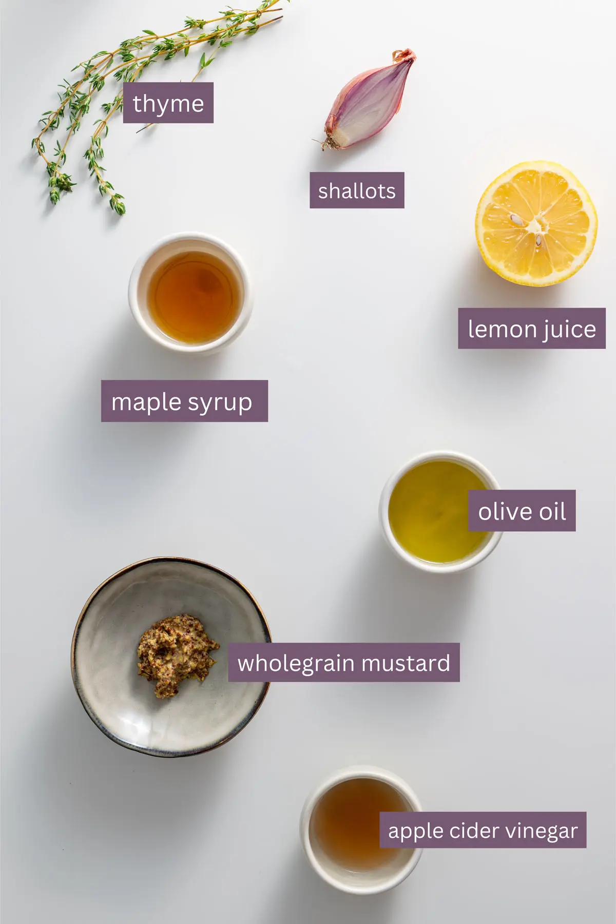 Ingredients for a mustard vinaigrette, including olive oil, maple syrup, shallots, lemon juice, thyme, and apple cider vinegar, labeled for clarity.