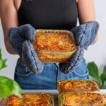 Sarah Cobacho holding a glass meal prep container filled with golden baked high-protein vegan lasagna.