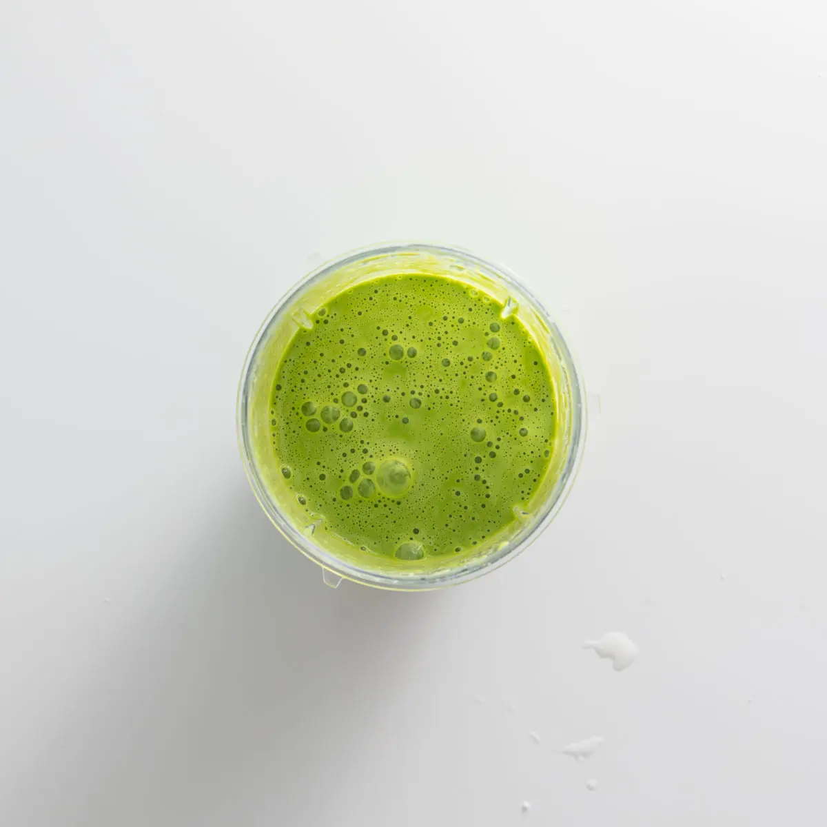 Blended green basil cream in a glass blender on a white surface.