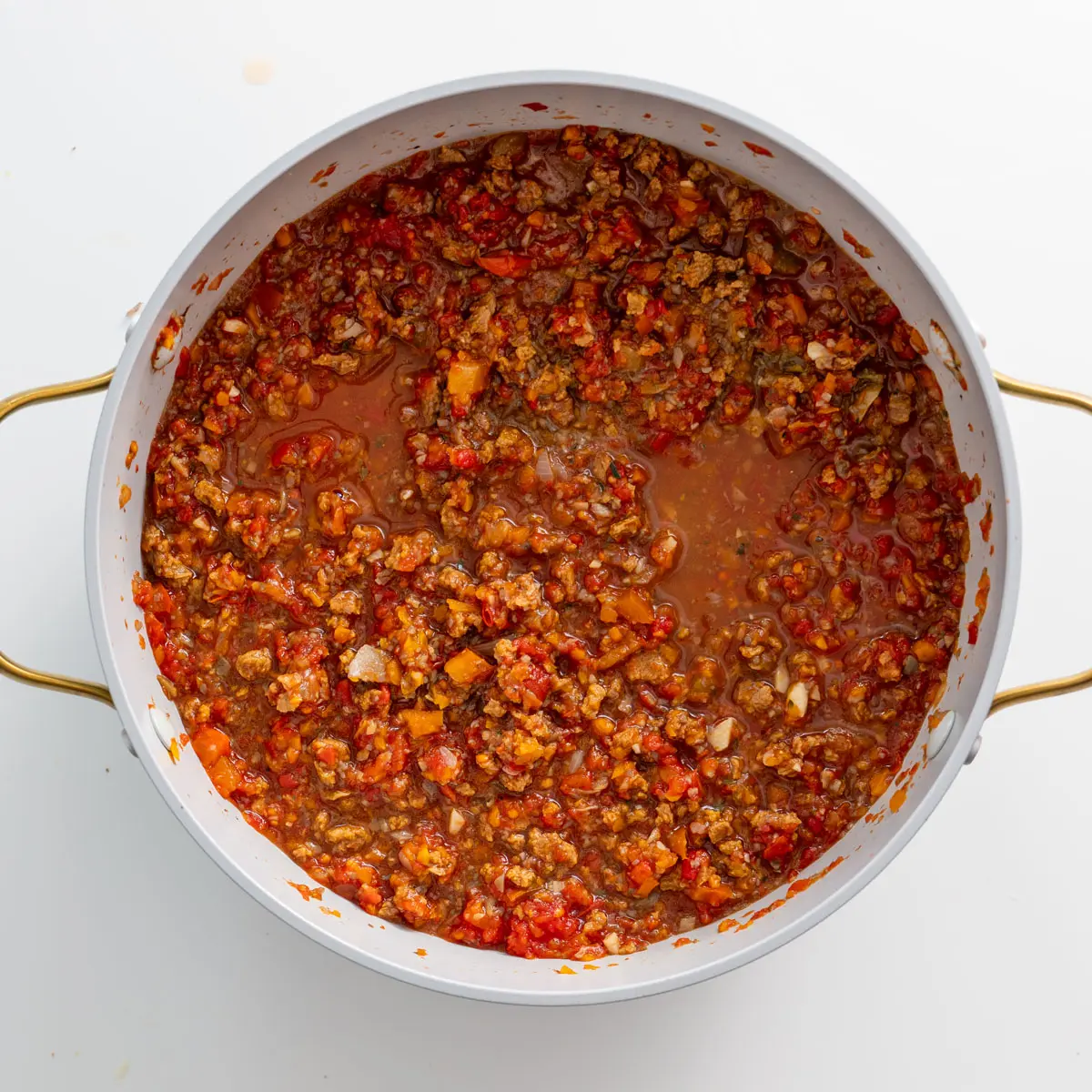 Cooked vegan bolognese sauce in a white pot with golden handles, showing a mix of textured vegetable protein and vegetables.