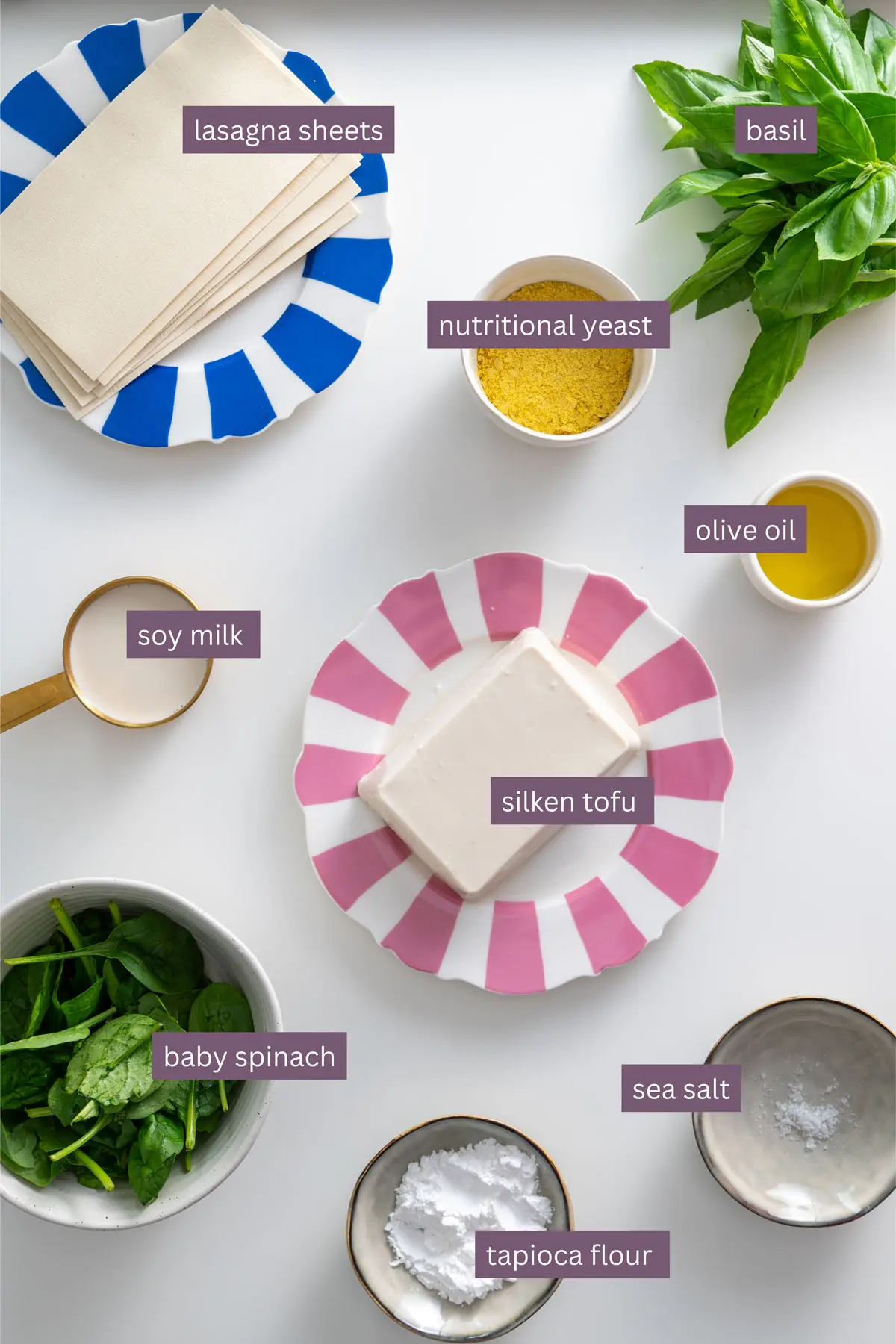 Vibrant ingredients for high-protein vegan lasagna arranged on a white surface, including lasagna sheets, silken tofu, spinach, and basil.
