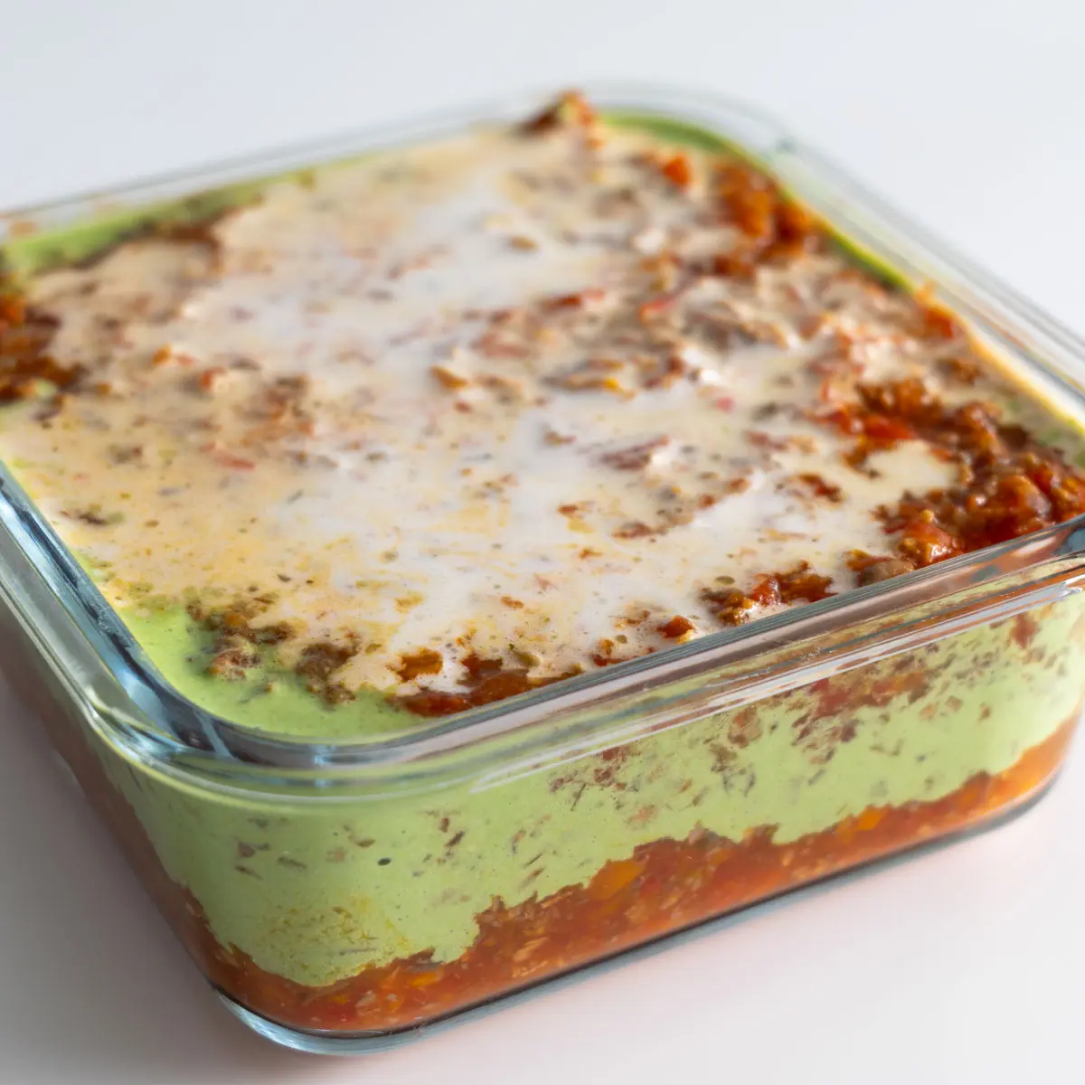High-protein vegan lasagna in a glass meal prep container, highlighting the creamy basil layer and tomato sauce.
