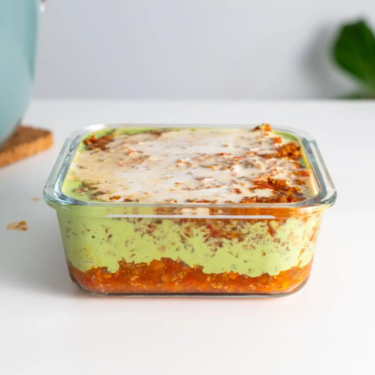 Glass meal prep container of layered high-protein vegan lasagna, highlighting the creamy basil and tomato layers.