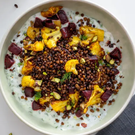 Close-up of roasted cauliflower, crispy lentils, and beetroot on a creamy tzatziki base in a green bowl.