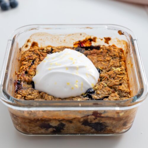 Close-up of baked blueberry oats topped with a dollop of coconut yogurt and lemon zest.