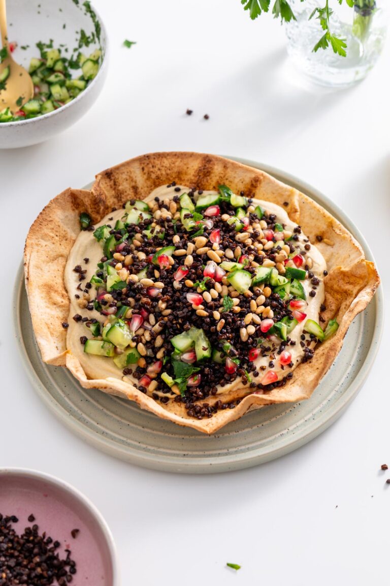 Freshly baked pita bowl filled with hummus, topped with cucumber salad, lentils, and pine nuts.