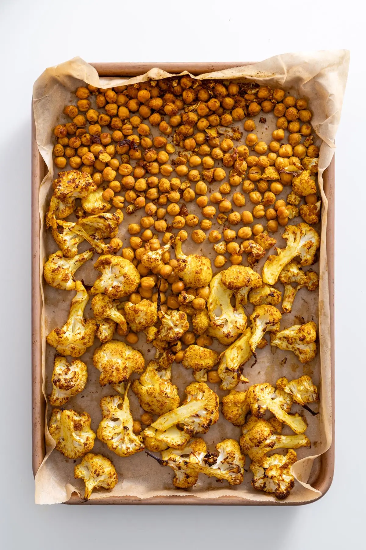 A baking tray with roasted chickpeas and cauliflower, golden brown from the tandoori spice blend.